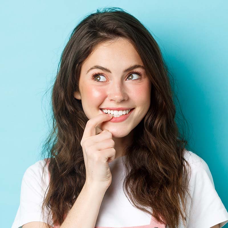 Thoughtful silly girl with cute curly hairstyle, biting finger and looking left at promo logo, smiling thinking about tasting ot trying something, standing over blue background.